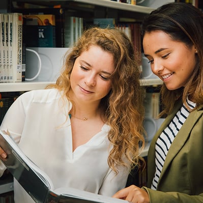 dos alumnas leyendo un libro en biblioteca