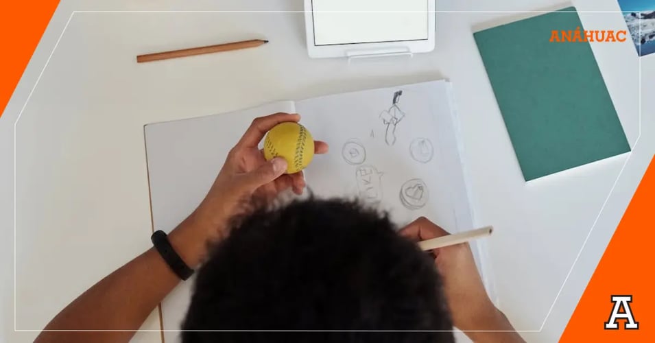 estudiante haciendo un bosquejo de una pelota de baseball mientras la sostiene con la mano izquierda