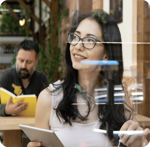 Estudiante de maestría utilizando una tablet en una cafetería moderna, representando el aprendizaje flexible y tecnológico de Posgrados Anáhuac