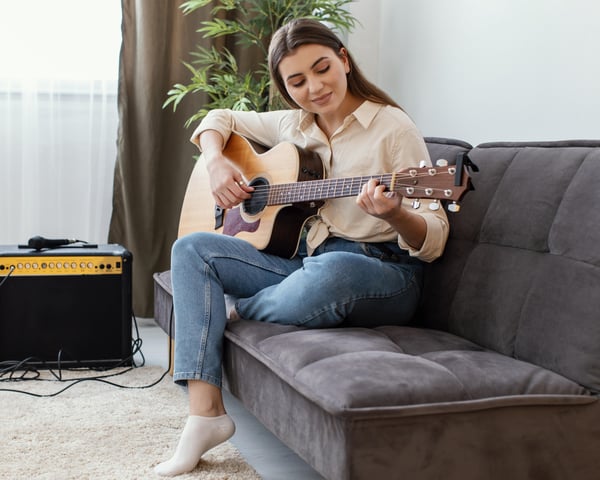 side-view-female-musician-home-playing-acoustic-guitar-while-sitting-sofa