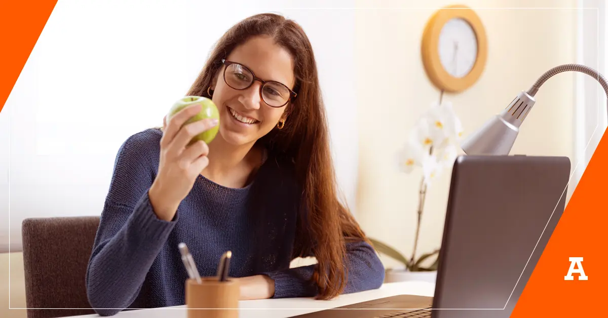 Licenciada en nutrición frente a su escritorio sostiene en su mano una manzana verde mientras sonríe