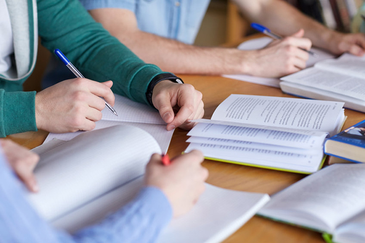 manos escribiendo y libros abiertos sobre una mesa